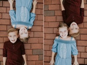 brother and sister laying on a brick walkway head to head